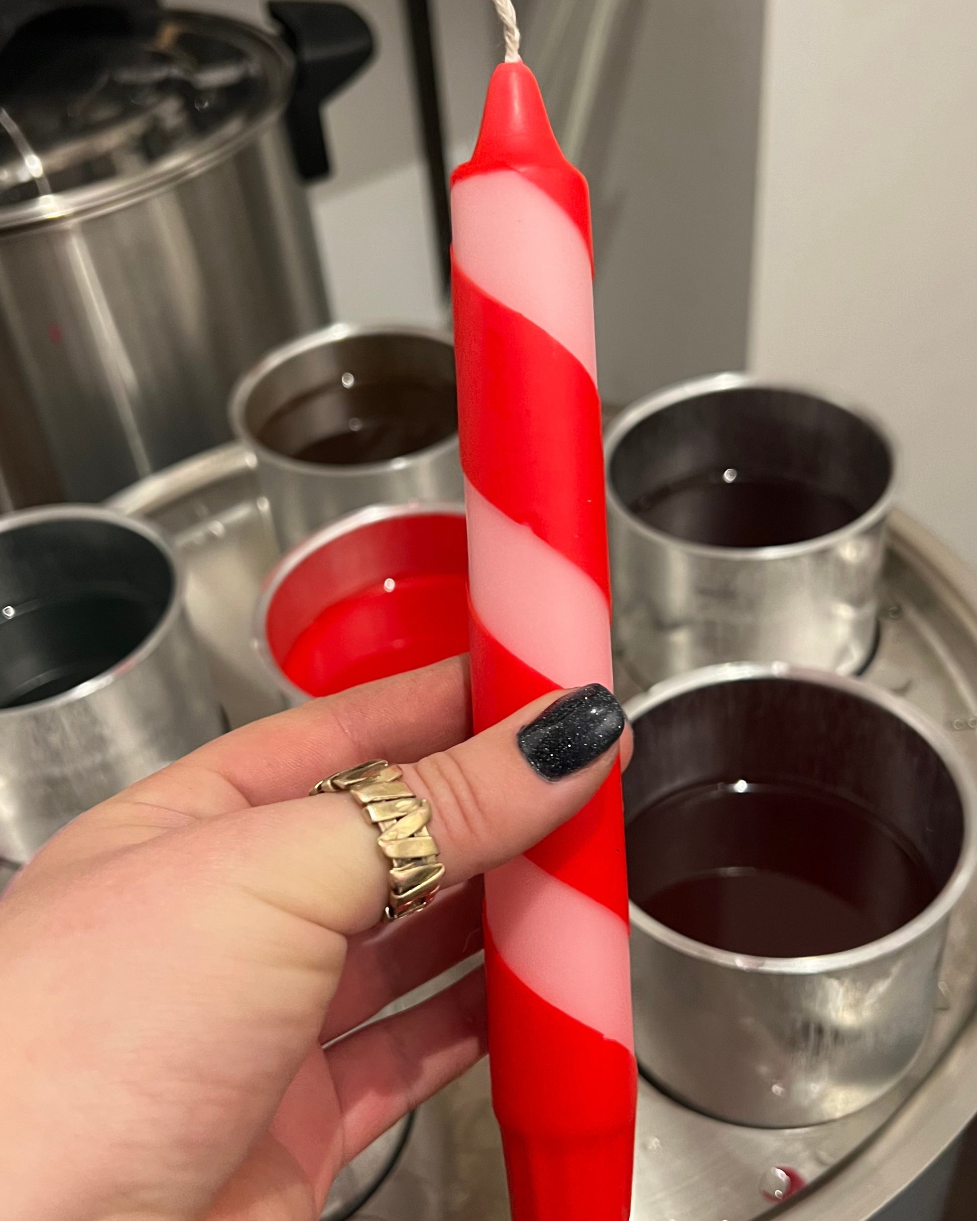 Candy cane design candle hold by a hand in a workshop setting