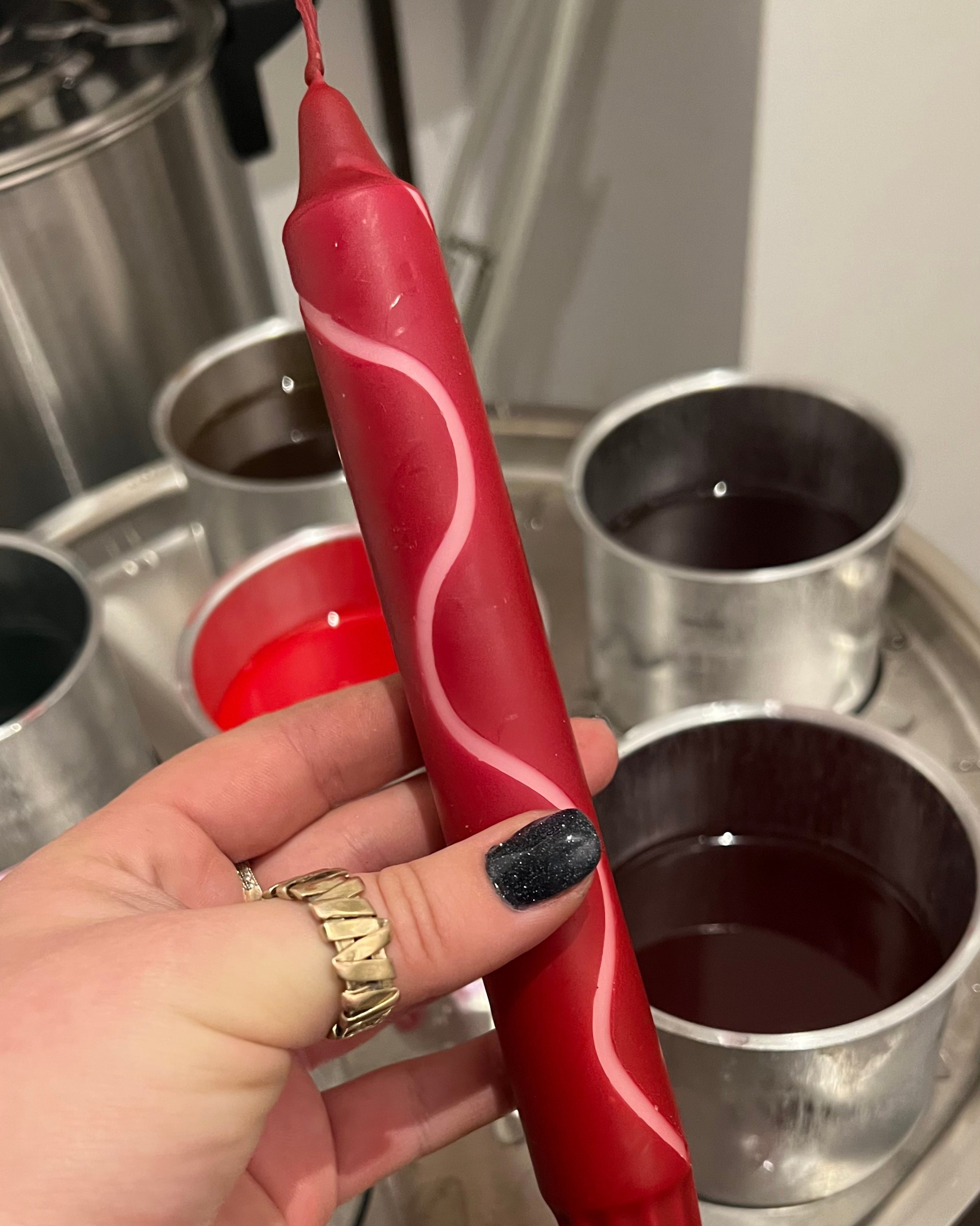 A swirly candle held by a hand in front of wax melting machine